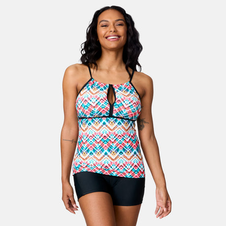 A woman with long, wavy hair smiles while wearing the Clearance Women's Zigzag Zest 2-in-1 Keyhole Tankini Top and black swim shorts, standing against a plain light gray background.