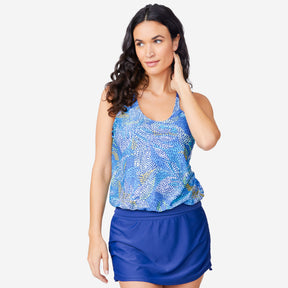 A woman models the Clearance Women's Fresco Double Strap Cut Out Blouson Tankini Top in a blue pattern with a solid blue skirt, standing against a white background and looking to the side with one hand near her neck.