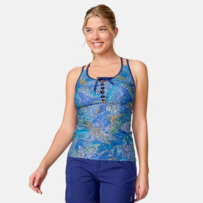 A woman smiles in the Clearance Women's Fresco Lace-Up Racerback Tankini Top with matching blue shorts, offering UPF 50+ sun protection, standing against a plain white background.