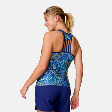 A woman with blonde hair in a ponytail models the Clearance Women's Fresco Lace-Up Racerback Tankini Top and navy shorts, smiling and turned to the side against a plain light background.