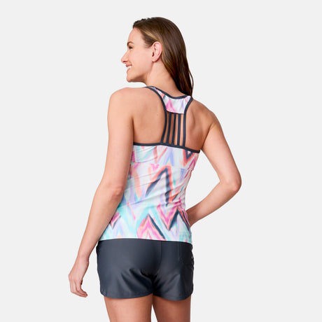 A woman smiles and faces away, wearing the Clearance Women's Oasis Chevron Lace-Up Racerback Tankini Top with a strappy back design and dark shorts, standing against a plain white background.