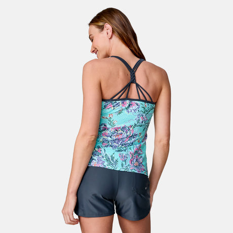 A woman with long brown hair smiles as she models the Clearance Women's Mosaic Garden Macrame Back Tankini Top and dark gray swim shorts, turned slightly to display the strappy, quick-drying top against a plain light background.