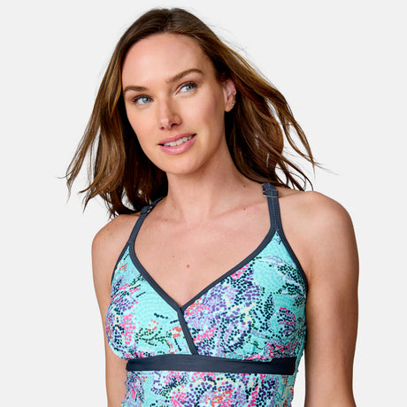 A woman with light brown hair wears the Clearance Women's Mosaic Garden Macrame Back Tankini Top, featuring a colorful pattern and dark trim, as she smiles softly against a light background. The quick-drying fabric ensures all-day comfort and style.