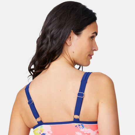 A woman with wavy dark hair is shown from behind wearing the Clearance Women's Poolside Bouquet Double Strap Tankini Top with blue adjustable straps and a pink floral pattern, made from quick-dry material, against a white background.
