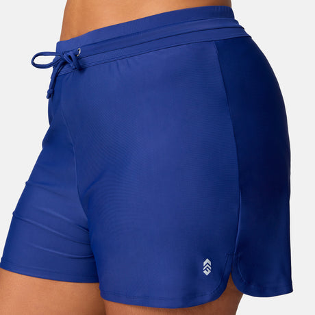 Close-up of a person wearing Free Country Women's Plus Size Drawstring Swim Short in royal blue, featuring a drawstring waistband, small white logo near the hem, and quick-dry comfort for active days by the water.