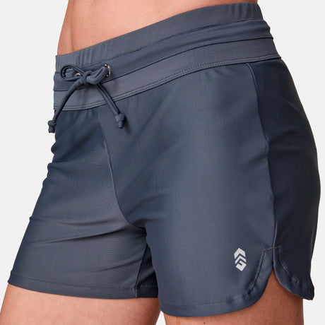 Close-up of a person wearing Free Country Women's Drawstring Swim Short in dark gray, featuring a drawstring waist and a small white logo near the left hem.