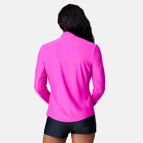 A woman with long dark hair faces away, wearing the Free Country Women's Sun Breeze 1/2 Zip Sunshirt in bright pink and black shorts against a plain white background.