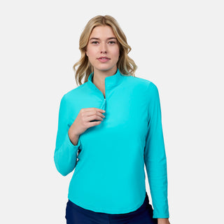 A woman with wavy blonde hair wears the Free Country Women's Sun Breeze 1/2 Zip Sunshirt, a bright turquoise moisture-wicking top, standing against a plain light background.