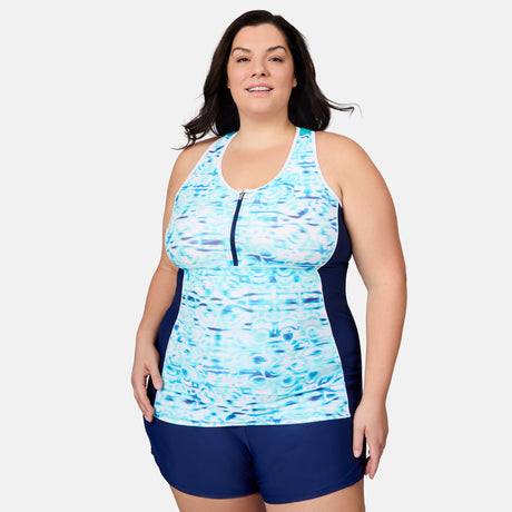 [Melissa is 5'10" wearing size 1X] Woman wearing a blue and white patterned tankini top with navy shorts on a light gray background