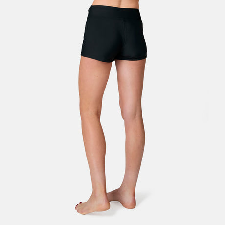 A person stands barefoot on a white background, shown from the waist down and facing away, wearing the Free Country Women's Fully Lined Swim Skort with UPF 50+ protection.