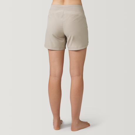[Model is wearing a size Small.] Woman wearing Free Country Women's 5" Bermuda Board Short in Sand, size S, made from quick drying UPF stretch performance fabric featuring a fly front zipper closure with a drawcord and two front pockets 