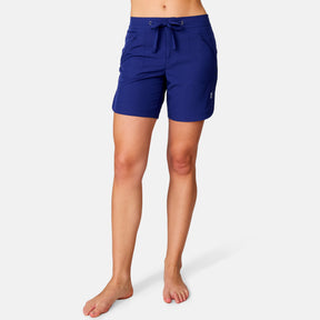 [Model is wearing a size Small.] Woman wearing Free Country Women's 7" Bermuda Board Short in Marine, size S, made from quick drying UPF stretch performance fabric featuring a fly front zipper closure with a drawcord and two front pockets 