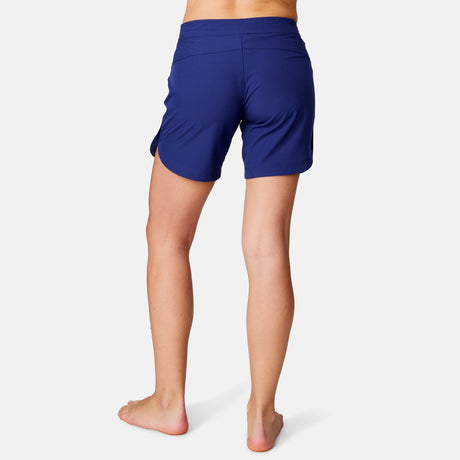 [Model is wearing a size Small.] Woman wearing Free Country Women's 7" Bermuda Board Short in Marine, size S, made from quick drying UPF stretch performance fabric featuring a fly front zipper closure with a drawcord and two front pockets 
