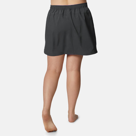 A person is standing barefoot, viewed from behind, wearing the Free Country Women's Plus Size Beach and Beyond Skort with an elastic waistband and four-way stretch against a plain white background.