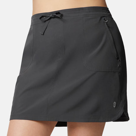 A close-up of a person wearing the Free Country Women's Plus Size Beach and Beyond Skort in dark gray, showing its drawstring waist, zippered side pocket, four-way stretch fabric, and a small logo by the hem.