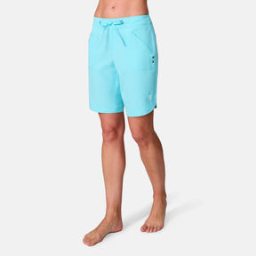 A woman is wearing the Women's Bermuda Board Short II in light blue, featuring quick-dry fabric, front pockets, and a drawstring waist, standing barefoot against a white background.