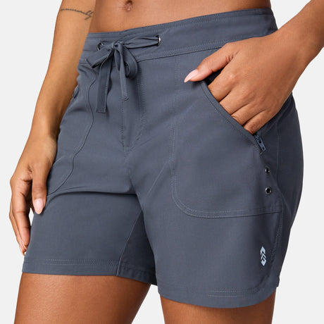 [Model is wearing a size Small.] Woman wearing Free Country Women's 5" Bermuda Board Short in Shadow, size S, made from quick drying UPF stretch performance fabric featuring a fly front zipper closure with a drawcord and two front pockets 