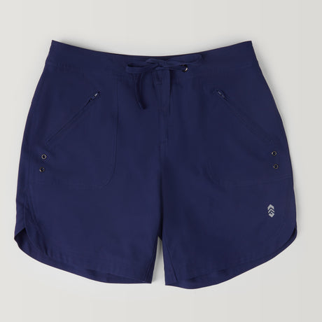 The Free Country Women's 7" Bermuda Board Short in navy features a drawstring waist, two front zippered pockets, metal grommets, subtle left-leg logo, quick dry fabric, and UPF 50+ protection, shown on a plain light background.