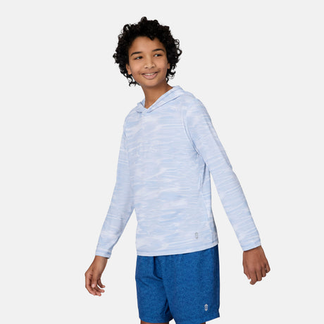 A smiling boy with curly hair wears The Kids' Everybody SunFree UPF Hoodie by Free Country in light blue, paired with blue shorts. He stands against a plain white background, looking left and ready for stylish sun protection.