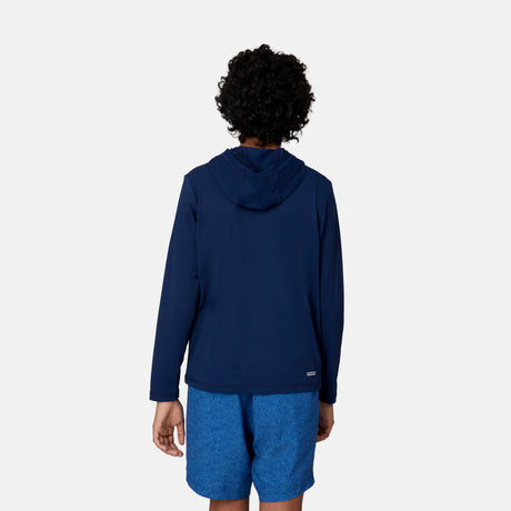 A child with short curly hair wears the Free Country Kids' Everybody SunFree UPF Hoodie in navy blue, made from recycled polyester, paired with blue shorts, standing with their back to the camera against a plain white background.
