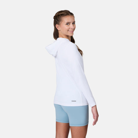 A girl with long brown hair in a braid smiles over her shoulder, wearing the Free Country Kids' Everybody SunFree UPF Hoodie and light blue shorts, standing against a plain light background.