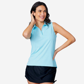 A woman smiles with one hand behind her head, modeling the Free Country Women's SunFree Sleeveless Top in light blue with UPF 50+ protection and a black skirt against a plain white background.