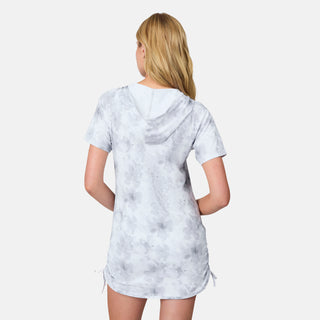 A woman with long blonde hair is shown from the back against a plain white background, wearing the Free Country Women's SunFree UPF Dress—a short-sleeve, hooded light gray tie-dye dress featuring adjustable drawstrings on the sides. This anti-odor summer dress delivers both style and freshness, making it perfect for warm days.