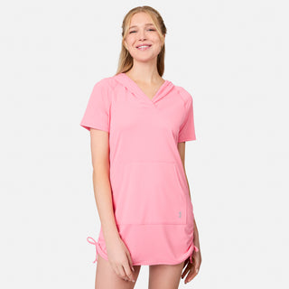A woman wearing the Free Country Women's SunFree UPF Dress in light pink, featuring short sleeves, a hood, and a front pocket, stands smiling against a plain white background. Made from recycled polyester, this cover-up offers UPF 50+ sun protection—perfect for staying comfortable and stylish on sunny days.