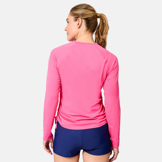 A woman with blonde hair in a ponytail is seen from behind, wearing the Free Country Women's SunFree Quarter Zip UPF Sunshirt in bright pink and dark blue shorts, against a plain white background.