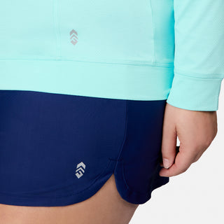 A person wearing the Free Country Women’s Plus Size SunFree UPF Hoodie in light blue and navy blue athletic shorts. Only the lower torso and part of the left arm are visible. Both garments feature small geometric logos and are crafted from moisture-wicking fabric for all-day comfort.