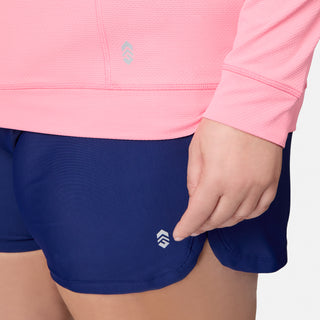 A person is wearing the Free Country Women's Plus Size SunFree UPF Hoodie in light pink, featuring a small chevron-style logo. This long-sleeve hoodie offers UPF 50+ sun protection, making it ideal for outdoor activities.