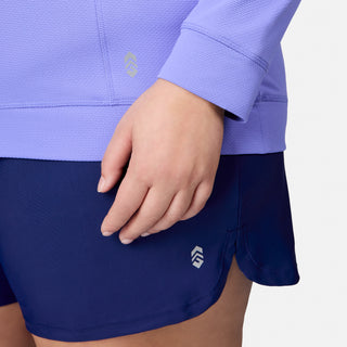 A person is wearing the Free Country Women's Plus Size SunFree UPF Hoodie in light purple, featuring a small geometric logo and moisture-wicking fabric for all-day comfort. Only their hand and part of the hoodie are visible.