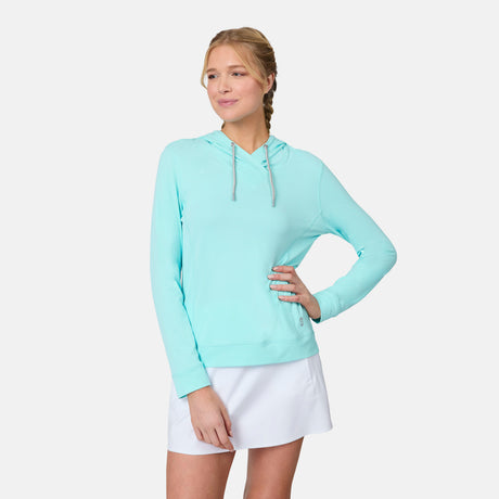 A blonde woman with a braid wears the Free Country Women's SunFree UPF Hoodie in light blue and a white skirt, standing with one hand on her hip against a plain white background.