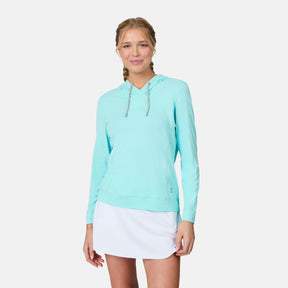 A woman with blonde braided hair wears the Free Country Women's SunFree UPF Hoodie in light blue and a white skirt, standing and smiling against a plain white background.