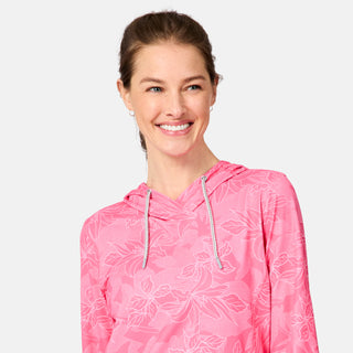 A woman with light brown hair smiles, wearing the Free Country Women's SunFree UPF Hoodie in a pink floral pattern with a drawstring. She stands against a plain light gray background.