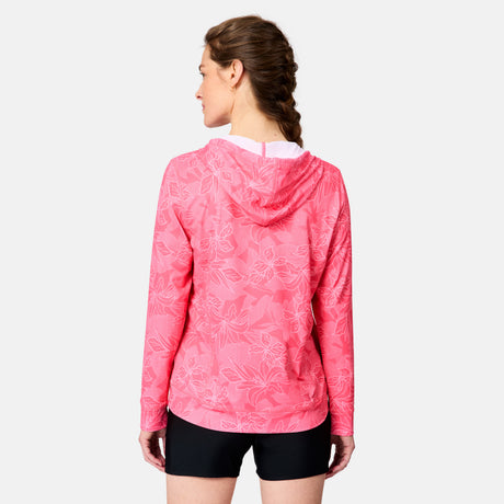 A woman with brown braided hair wears the Free Country Women's SunFree UPF Hoodie in pink with a floral pattern, paired with black shorts. She stands facing away from the camera against a plain white background.
