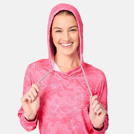 A smiling person wears the Free Country Women's SunFree UPF Hoodie with the hood up, holding the drawstrings and looking at the camera, set against a plain light background.
