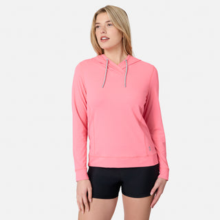 A woman in a light pink Free Country Women's SunFree UPF Hoodie and black shorts stands against a plain white background, looking slightly to her left with a relaxed expression.