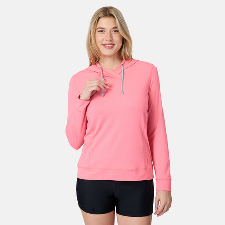 A smiling woman with long blonde hair wears the Free Country Women's SunFree UPF Hoodie in pink and black shorts, standing against a plain light gray background.
