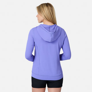 A woman with straight blonde hair is seen from the back wearing the Free Country Women's SunFree UPF Hoodie in lavender and black shorts, standing against a plain white background.