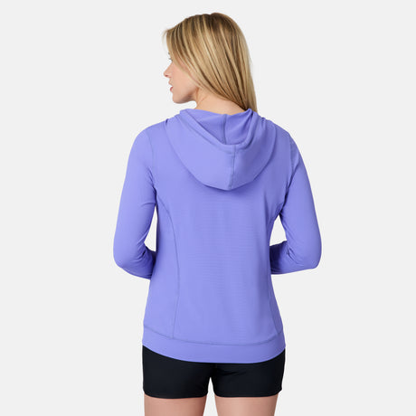 A woman with straight blonde hair is seen from the back wearing the Free Country Women's SunFree UPF Hoodie in lavender and black shorts, standing against a plain white background.