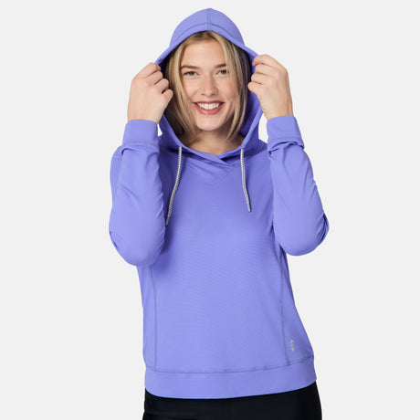 A smiling person wears the Free Country Women's SunFree UPF Hoodie in light purple with black pants, holding the hood with both hands against a plain white background.