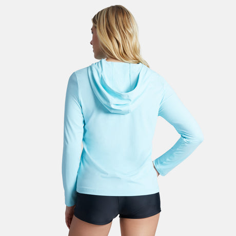 A woman with blonde hair wears the Free Country Women's SunFree Full Zip UPF Sunshirt in light blue and black shorts, standing with her back to the camera against a plain white background.