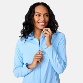 A woman with long, wavy dark hair smiles while zipping up the Free Country Women's SunFree Full Zip UPF Sunshirt. She looks to the side against a plain white background.