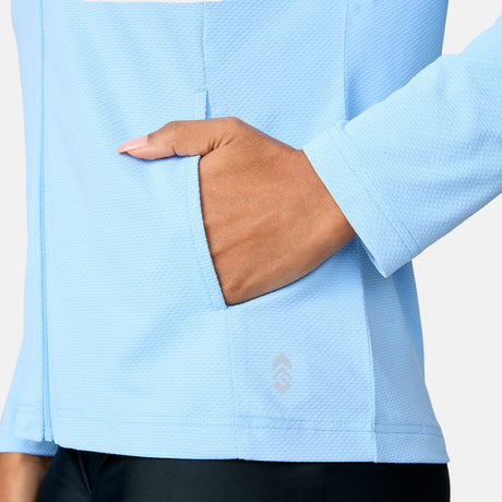 A woman wears the Free Country Women's SunFree Full Zip UPF Sunshirt in light blue, with her right hand in the front pocket; only her torso and arm are visible against a plain background.