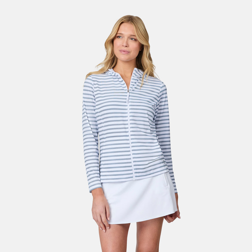 A woman wears the Free Country Women's SunFree Full Zip UPF Sunshirt in light blue and white stripes, featuring UPF 50+ sun protection, paired with a white skirt, standing against a plain background with a relaxed expression.