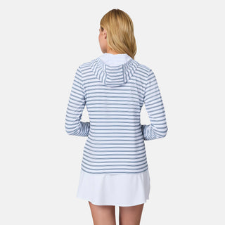 A woman with blonde hair stands facing away, wearing the Free Country Women's SunFree Full Zip UPF Sunshirt in light blue and white stripes over a white skirt. The sunshirt features a hood and is made from recycled fabric against a plain white background.