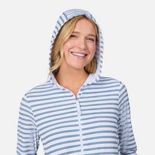 A smiling woman wears the Free Country Women's SunFree Full Zip UPF Sunshirt, a white and blue striped hooded top made from recycled fabric, standing against a plain white background.