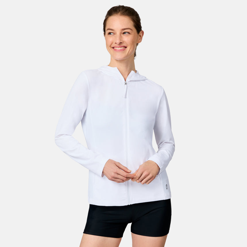 A woman smiles in the Free Country Women's SunFree Full Zip UPF Sunshirt, a white hooded jacket made from recycled fabric, paired with black shorts against a plain white background.