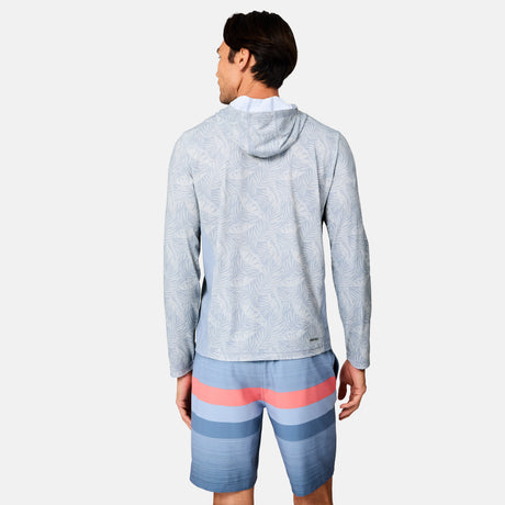 A man stands facing away, wearing the Free Country Men's SunFree UPF Printed Hoodie in light blue and blue shorts with pink and navy stripes against a plain white background.